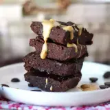 En stapel mörka protein brownies med en krämig topping och chokladknappar på en vit tallrik.