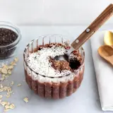 En skål med overnight oats chokladboll, toppad med kokosflingor. Bredvid finns ingredienser som havregryn, chiafrön och kakaopulver.