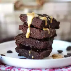 En stapel mörka protein brownies med en krämig topping och chokladknappar på en vit tallrik.
