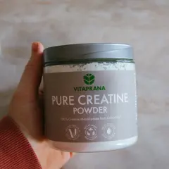 En hand håller en burk med Vitaprana Pure Creatine Powder. Kan vara ett komplement för den som vill ha hjälp med kreatin viktnedgång.