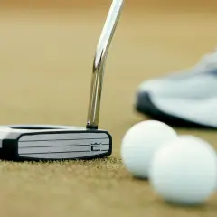 En golfare funderar vilken putter ska man ha. En modern putter ligger på greenen bredvid golfbollar, med en sko i bakgrunden.