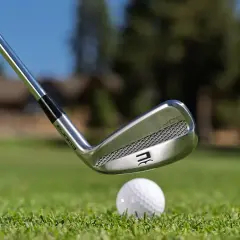En golfklubba av märket Cobra närmar sig en golfboll på en grön gräsmatta. Frågan om hur långa golfklubbor ska man ha är central för spelet.