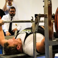 Man utför en floor press med tung vikt på stången. Domare ser på.