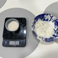 En digitalvåg visar 91 gram ris i en liten behållare. Bredvid står en skål med mer ris, redo att ätas. Perfekt för att hålla koll på råris kalorier.