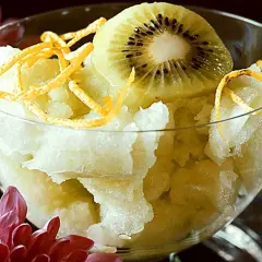 En skål med ljusgul sorbet, toppad med en skiva kiwi och strimlad apelsinskal. En svalkande vattenmelon sorbet för en varm dag.