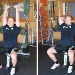 Man utför french press i gym. Han sitter på en bänk och håller en skivstång över huvudet.