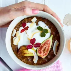 En skål med gröt, yoghurt, fikon och kokosflingor. En perfekt frukost med lite kalorier, serverad med en kopp te.