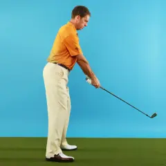 Man i orange pikétröja och beige byxor förbereder sig för ett golfslag. Hans svinghastighet kan påverkas av ålder.