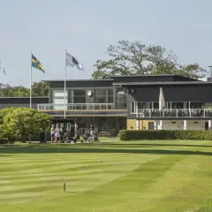 En golfklubb i Sverige med en modern byggnad, flaggor och välklippta fairways. Här kan man höra många golftermer.