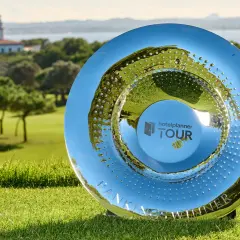 En glänsande pokal på en golfbana, med en fyr med hav i bakgrunden. Denna trofé symboliserar framgången i en **challenge tour**.