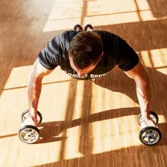 Man gör armhävningar med träningshjul på ett gymgolv.