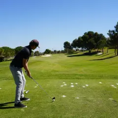 En man förbereder sig för ett slag på en golfbana. Han är klädd i en keps och tröja, redo för olika spelformer golf.