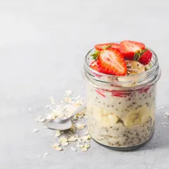 En burk med overnight oats recept toppad med jordgubbar och banan. En sked ligger bredvid med havregryn.