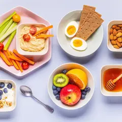En frukost med kolhydratrik mat: yoghurt med granola och blåbär, frukt, ägg, kex, nötter, honung och grönsaksstavar med hummus.