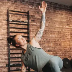 Kvinna med tatueringar utför en övning på sitt gymprogram. Hon ligger på sidan med en arm uppsträckt.