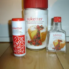 Tre förpackningar Suketter, ett sockerersättningsmedel, står på ett träbord. En burk, en tub och en flaska. Suketter är utmärkt till bakning och matlagning, helt utan kalorier.