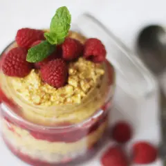 En burk med overnight oats med saffranssmak, toppad med hallon och mynta. En sked ligger bredvid.