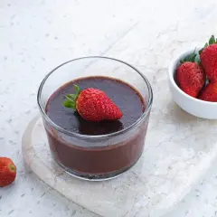 Chokladig proteinpudding i glas, toppad med jordgubbe. Bredvid en skål med färska jordgubbar. Ett enkelt recept på proteinpudding.