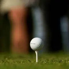 En golfboll i huvudet, redo för ett slag. Gräset är grönt och bakgrunden suddig.