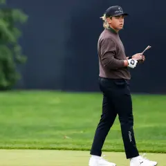 Golfare i brun tröja och keps går på banan, funderar på vad betyder vit markering på banan?