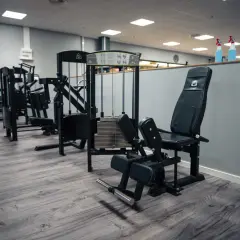 En adduktormaskin i ett modernt gym. Maskinen är svart med vadderade dynor och en viktstapel.