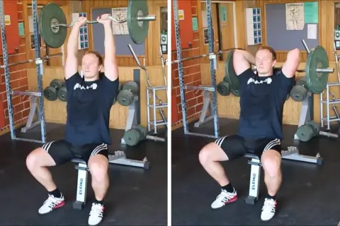 Man utför french press i gym. Han sitter på en bänk och håller en skivstång över huvudet.