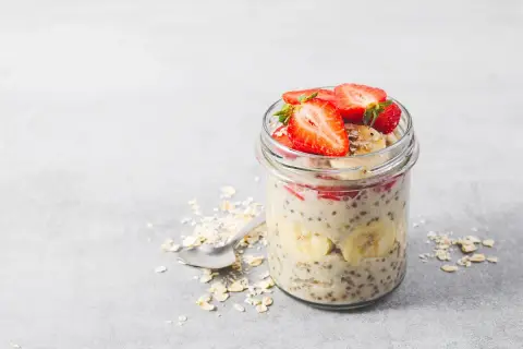 En burk med overnight oats recept toppad med jordgubbar och banan. En sked ligger bredvid med havregryn.