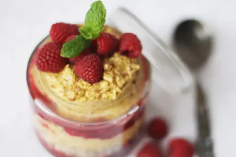 En burk med overnight oats med saffranssmak, toppad med hallon och mynta. En sked ligger bredvid.