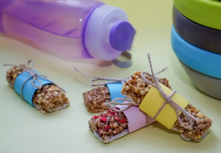 Energibars med nötter och frukt, perfekta för snabba kalorier. En lila vattenflaska och en stapel skålar i bakgrunden.