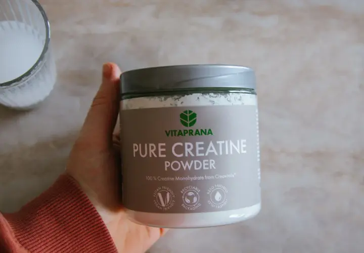 En hand håller en burk med Vitaprana Pure Creatine Powder. Kan vara ett komplement för den som vill ha hjälp med kreatin viktnedgång.