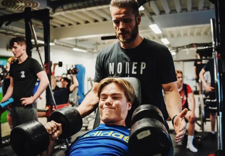 Tränare hjälper en ung man med hantlar, en riktig craze pwo-känsla i gymmet.