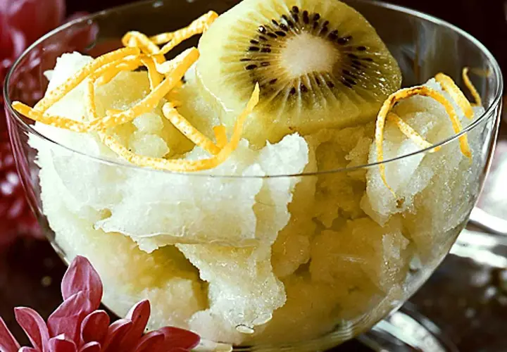 En skål med ljusgul sorbet, toppad med en skiva kiwi och strimlad apelsinskal. En svalkande vattenmelon sorbet för en varm dag.
