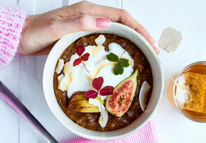 En skål med gröt, yoghurt, fikon och kokosflingor. En perfekt frukost med lite kalorier, serverad med en kopp te.