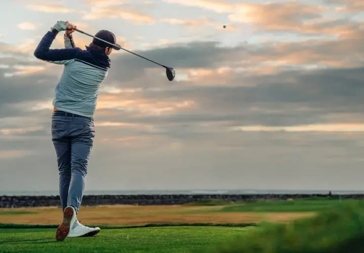 En golfare svingar klubban vid solnedgången. Ett perfekt sätt att använda sitt friskvårdsbidrag för golf.