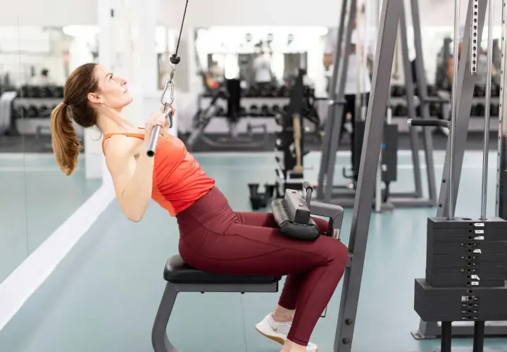 Kvinna tränar enarms latsdrag på gym.