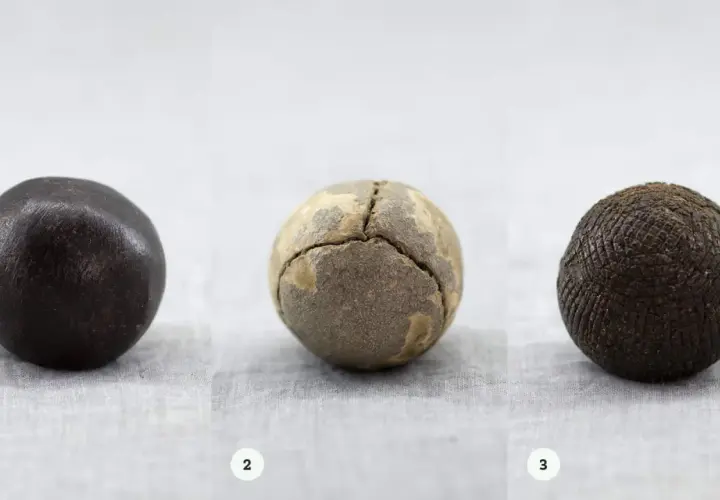 Tre gamla bollar: en mörk, en sprickig och en med rutmönster. Kanske en tidig guttaperka boll?