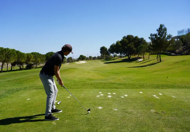 En man förbereder sig för ett slag på en golfbana. Han är klädd i en keps och tröja, redo för olika spelformer golf.