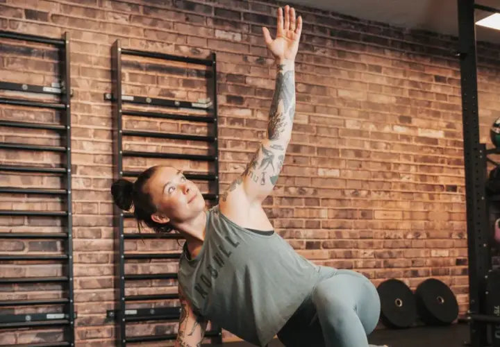 Kvinna med tatueringar utför en övning på sitt gymprogram. Hon ligger på sidan med en arm uppsträckt.