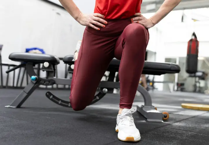 En person utför split squats i ett gym. En boxningssäck syns i bakgrunden.