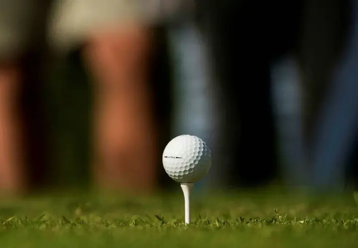 En golfboll i huvudet, redo för ett slag. Gräset är grönt och bakgrunden suddig.