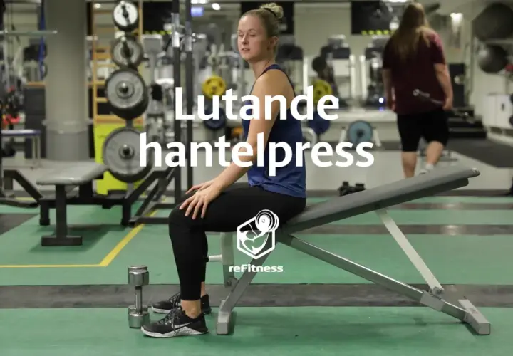 Kvinna förbereder sig för lutande hantelpress på gym. Hantlar ligger på golvet.