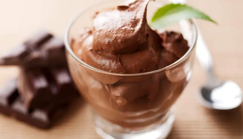 Chokladig kaseinpudding i ett glas, med chokladbitar och en sked i bakgrunden.