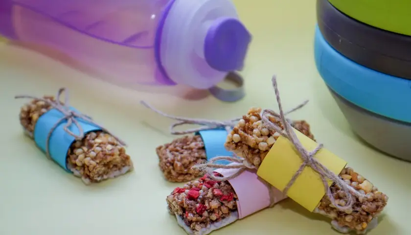 Energibars med nötter och frukt, perfekta för snabba kalorier. En lila vattenflaska och en stapel skålar i bakgrunden.