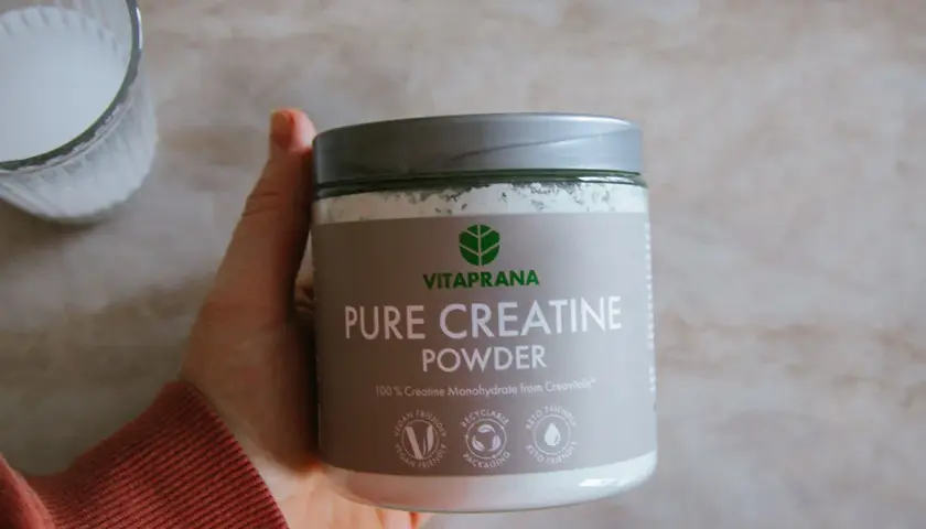 En hand håller en burk med Vitaprana Pure Creatine Powder. Kan vara ett komplement för den som vill ha hjälp med kreatin viktnedgång.