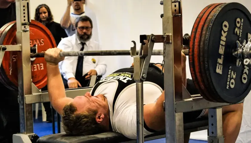 Man utför en floor press med tung vikt på stången. Domare ser på.