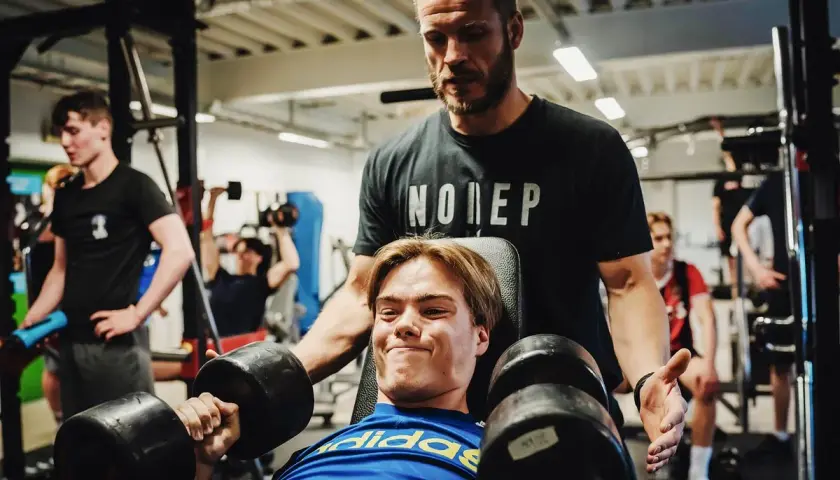 Tränare hjälper en ung man med hantlar, en riktig craze pwo-känsla i gymmet.