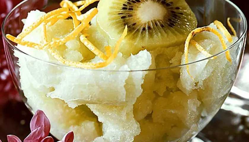 En skål med ljusgul sorbet, toppad med en skiva kiwi och strimlad apelsinskal. En svalkande vattenmelon sorbet för en varm dag.