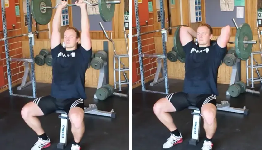 Man utför french press i gym. Han sitter på en bänk och håller en skivstång över huvudet.