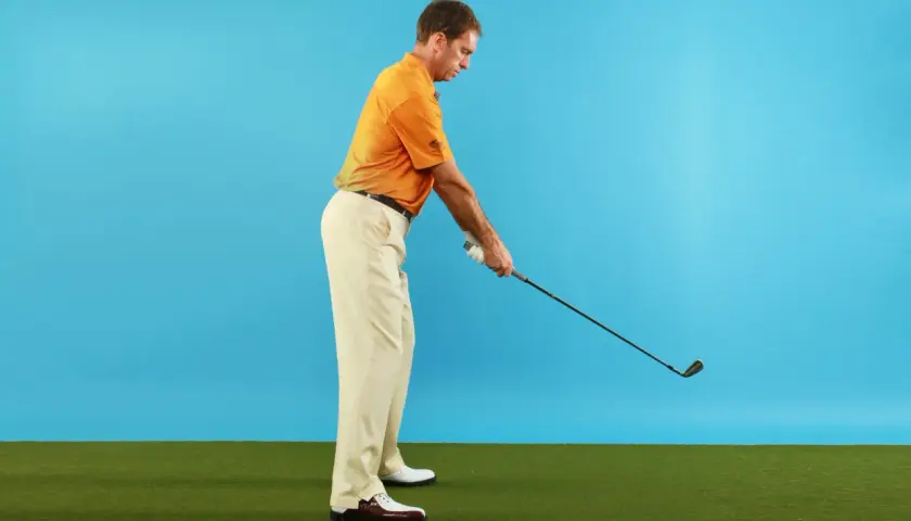 Man i orange pikétröja och beige byxor förbereder sig för ett golfslag. Hans svinghastighet kan påverkas av ålder.