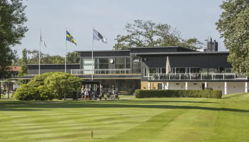 En golfklubb i Sverige med en modern byggnad, flaggor och välklippta fairways. Här kan man höra många golftermer.